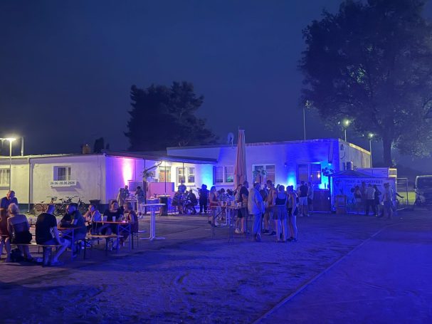 Menschenmengen in einem beleuchteten Außenbereich eines Veranstaltungsortes bei Nacht.