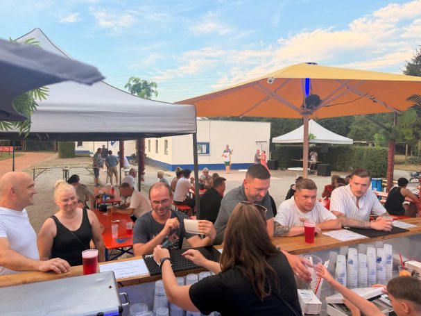 Menschen sitzen an einer Bar im Freien, genießen Getränke und unterhalten sich.