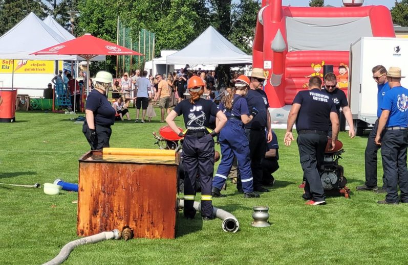 Feuerwehrleute in Einsatzkleidung bei einer Übung im Freien mit Ausrüstung und Zuschauern.