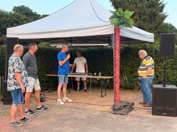 Vier Personen stehen unter einem Pavillon, eine Person spricht mit dem Mikro und ehrt den ausgeschiedenen Präsidenten.