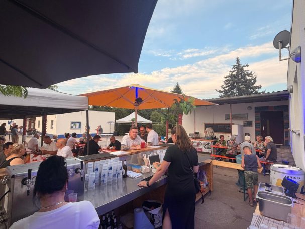 Bunter Außenbereich eines Restaurants mit Gästen und Sonnenschirmen unter blauem Himmel.