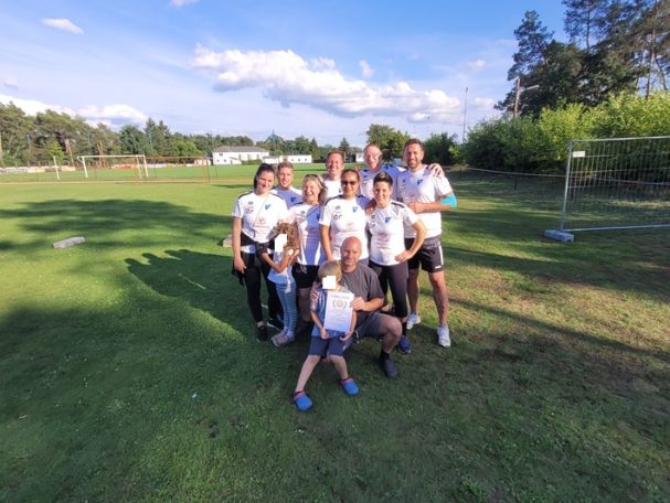Gruppe der sieben Spieler/innen in Sportkleidung auf einem grünen Feld, Sonne scheint.