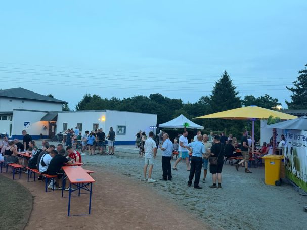 Menschen versammeln sich auf einem Festivalgelände mit Ständen und Tischen im Freien.