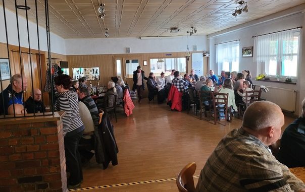 Menschen sitzen im Vereinsheim nach dem traditionellen Neujahrslauf. Der Raum ist hell und die langen Tische sind gut gefüllt
